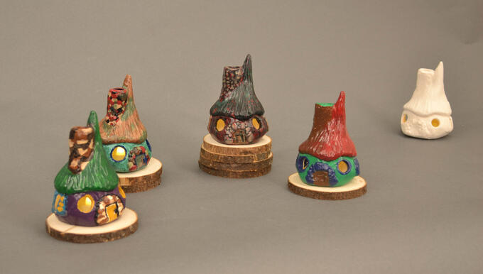 Five identical cottage houses painted differently. First is green, purple, and yellow. Second is brown, blue, and green. Third is green, black, and red. Fourth is red, green, and blue. Fifth in back is white.