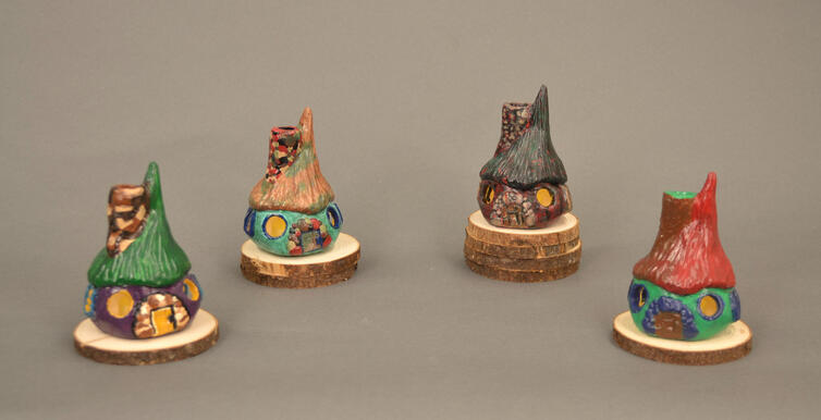 Four identical cottage houses painted differently. First is green, purple, and yellow. Second is brown, blue, and green. Third is green, black, and red. Fourth is red, green, and blue.