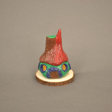 Small cottage made out of clay. A red and brown roof, brown chimney and door. green body with dark blue detailing.