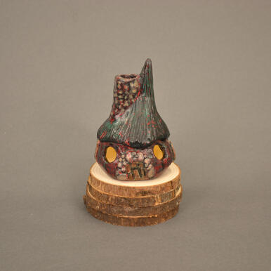 Mini cottage with dark green roof, red/green/black body, grey stone door and chimney with red splatter.