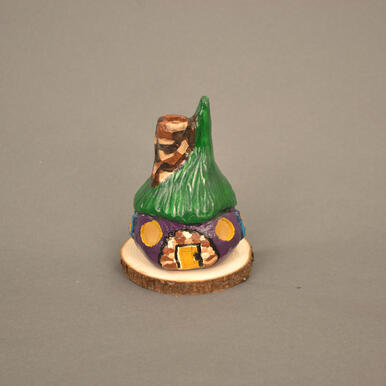 Small cottage made of clay. A green roof with a purple body with blue/yellow detailing. Dark/medium/light brown detailing on door and chimney.